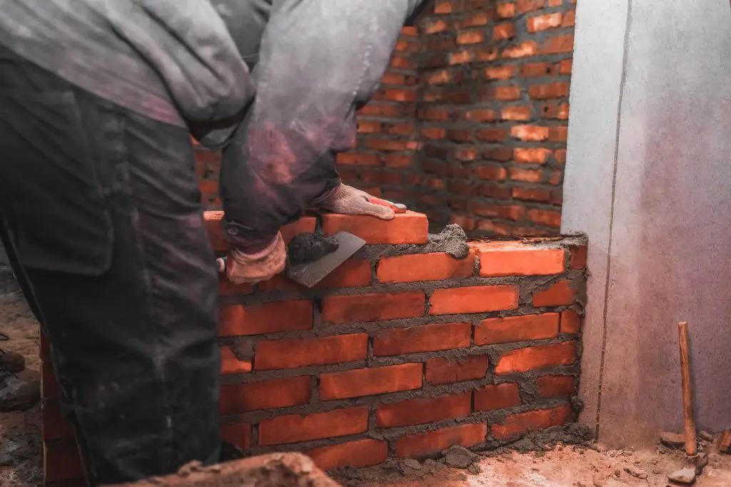 Bricklayer puts bricks to make a wall